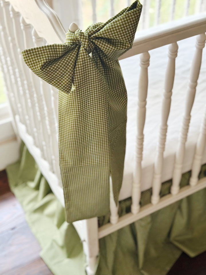 Close-up of a green gingham crib bow sash with long tails over the crib skirt