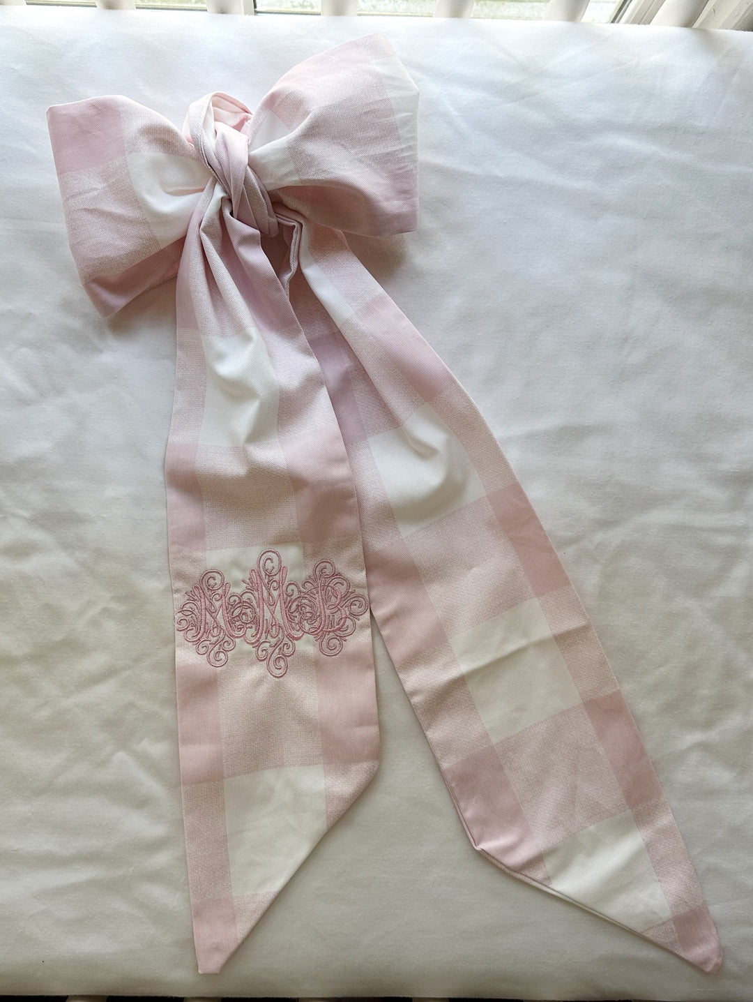 The bow laid flat showing the full sash length, the pink monogram and the angled-cut tail ends