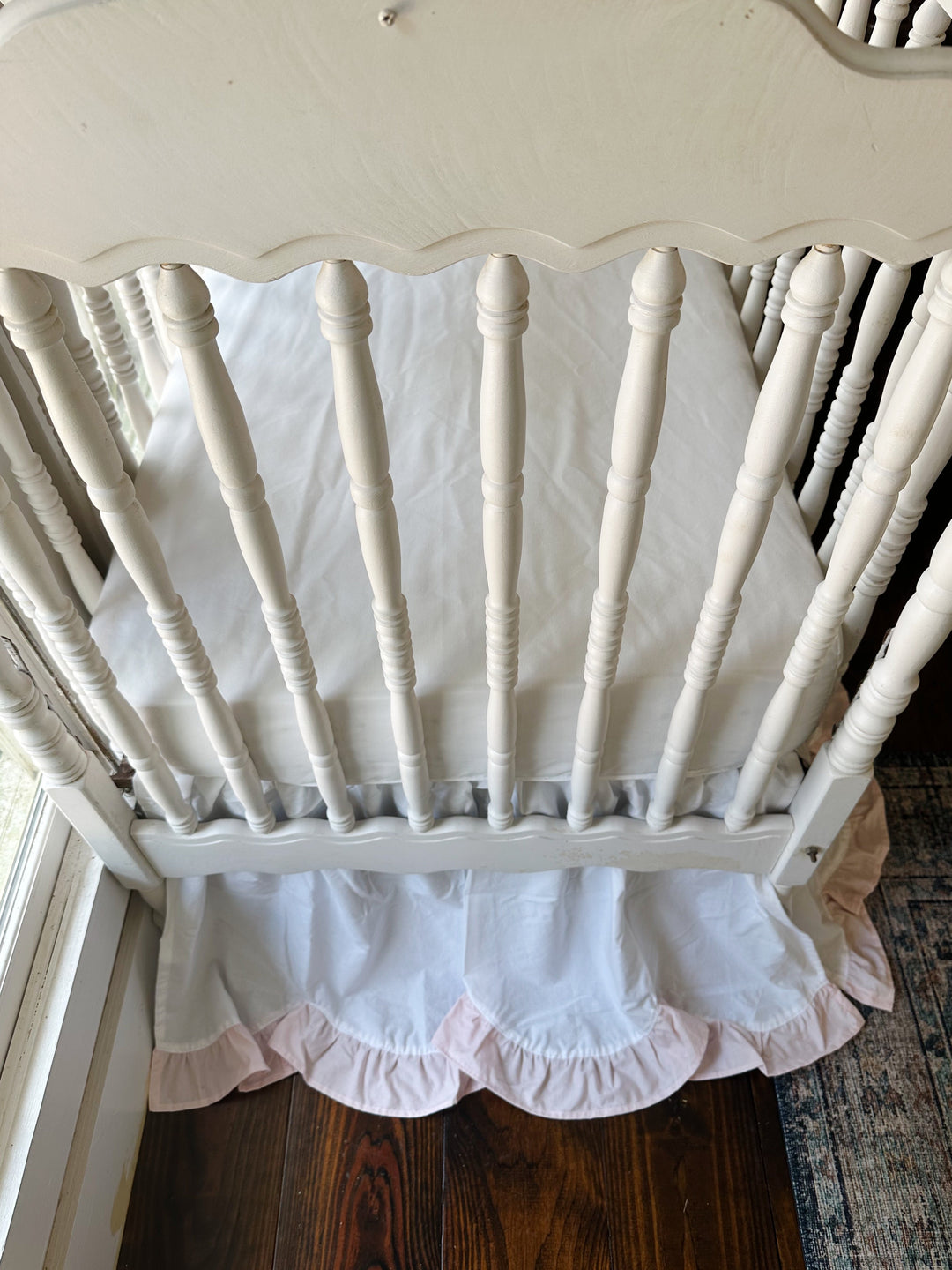 Scalloped crib headboard above the gathered white skirt and its baby pink scalloped ruffle