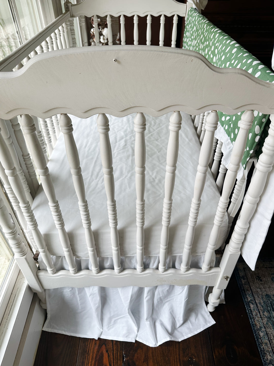 Looking down past the scalloped headboard at the white sheet and gathered white skirt