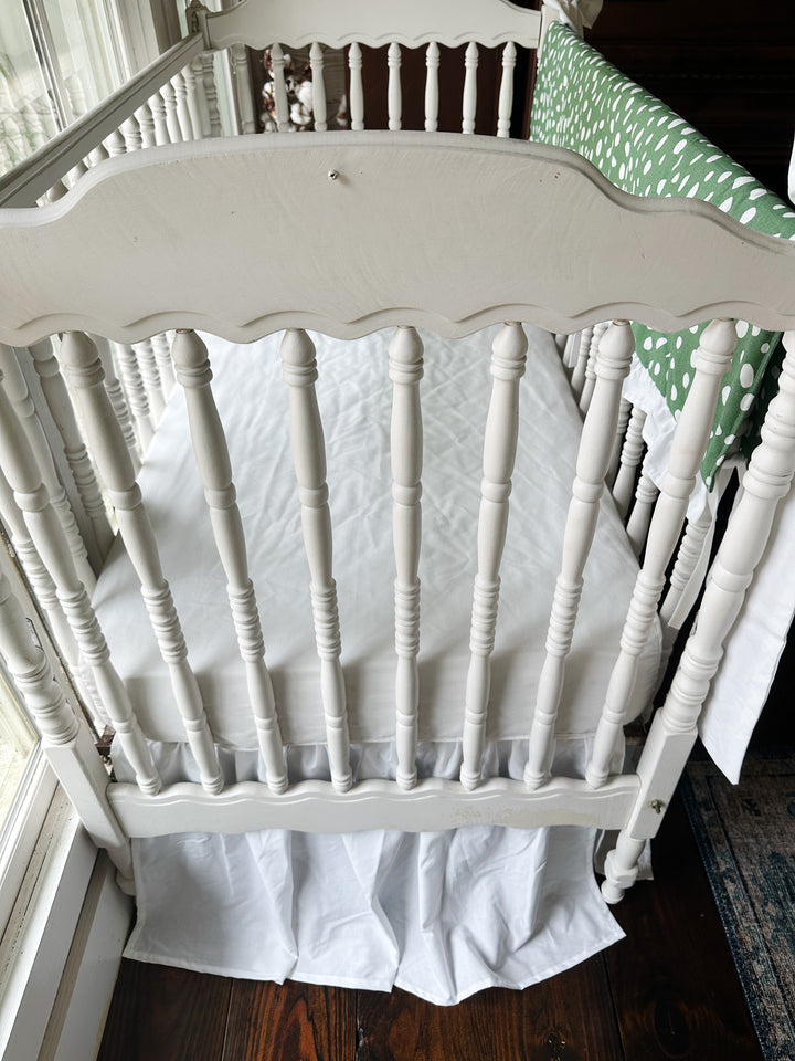 Looking down past the scalloped headboard at the white sheet and gathered white skirt