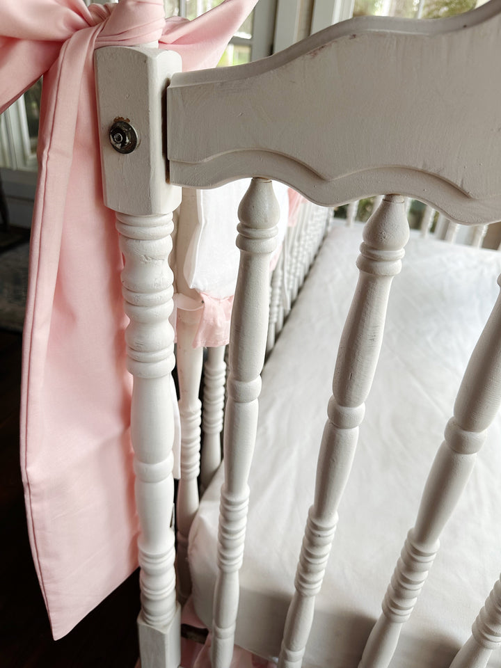 Large Sisters Pink cotton crib bow tied in a full knot at the corner of a white crib