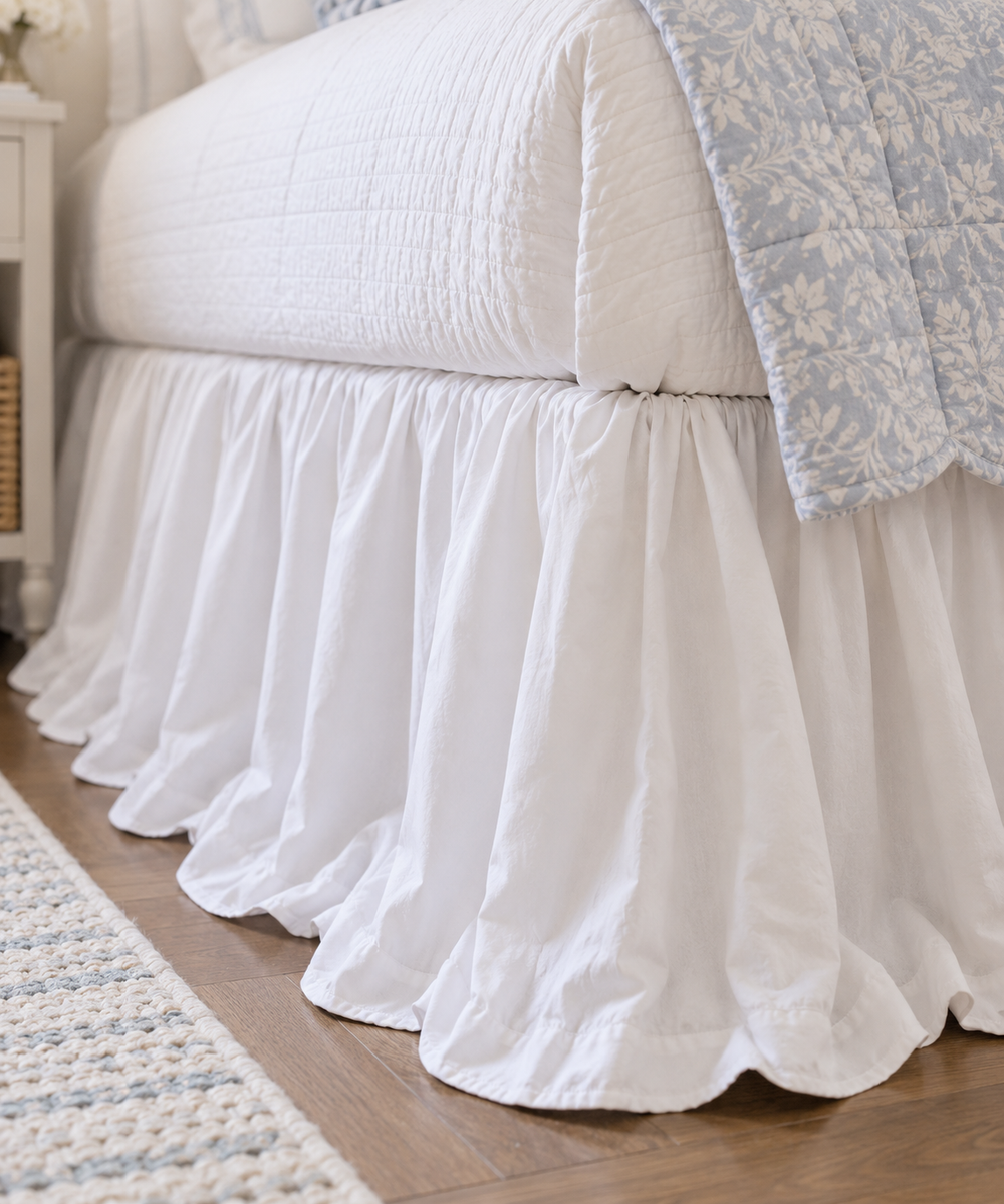 Close up of the deep gathers and ruffled hem on a white cotton twin bed skirt over a wood floor - High Cotton Textile