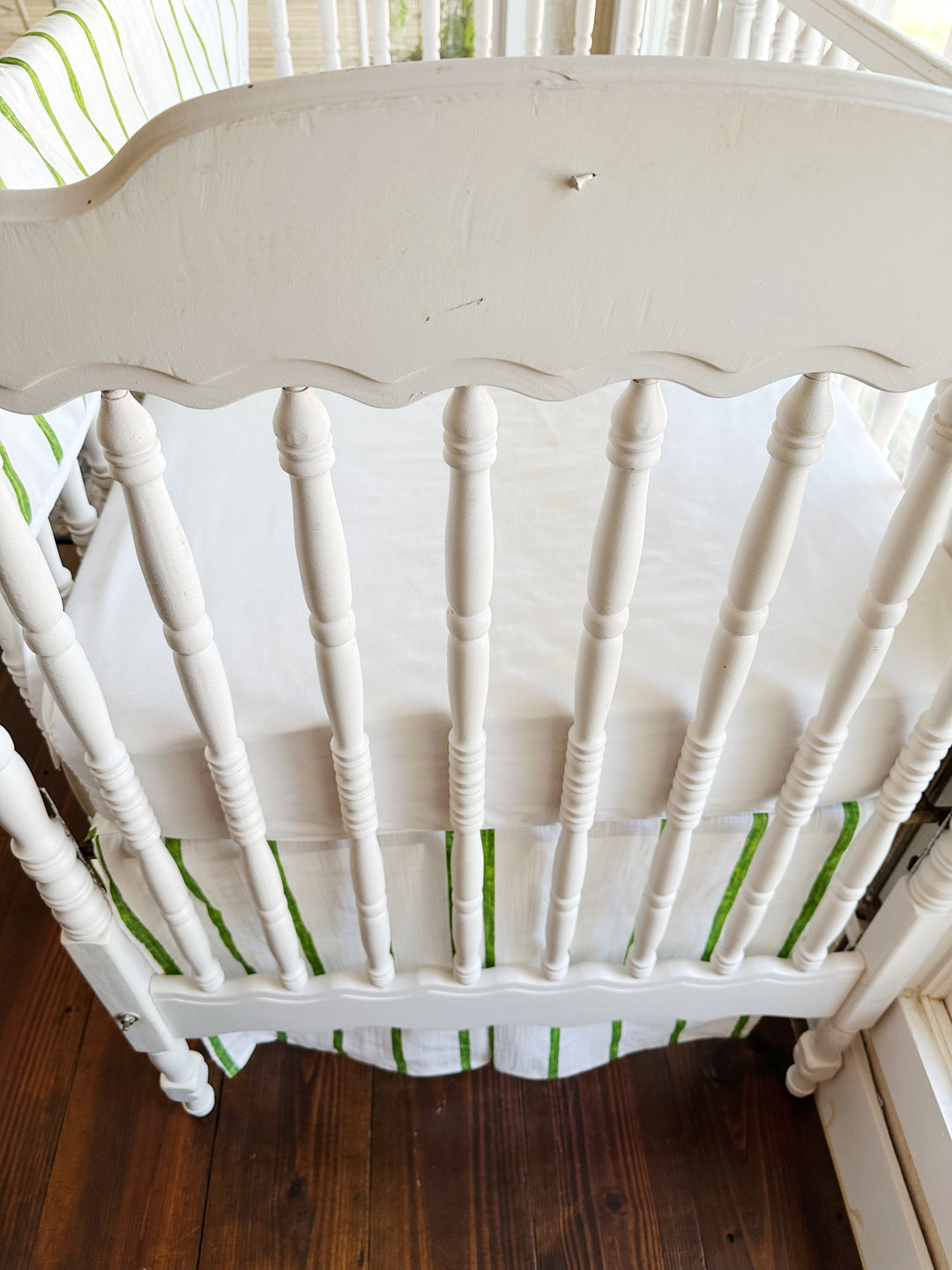 The scalloped headboard and turned spindles above the green striped tailored skirt