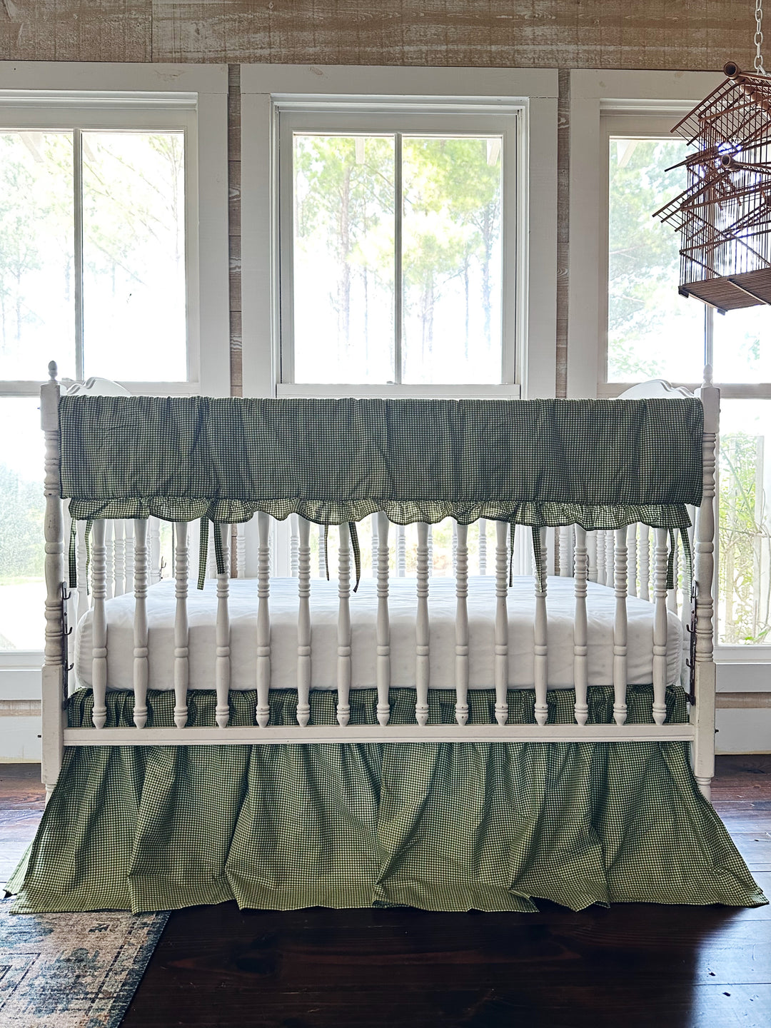 Pine green gingham crib rail cover and farmhouse crib skirt on a white spindle crib