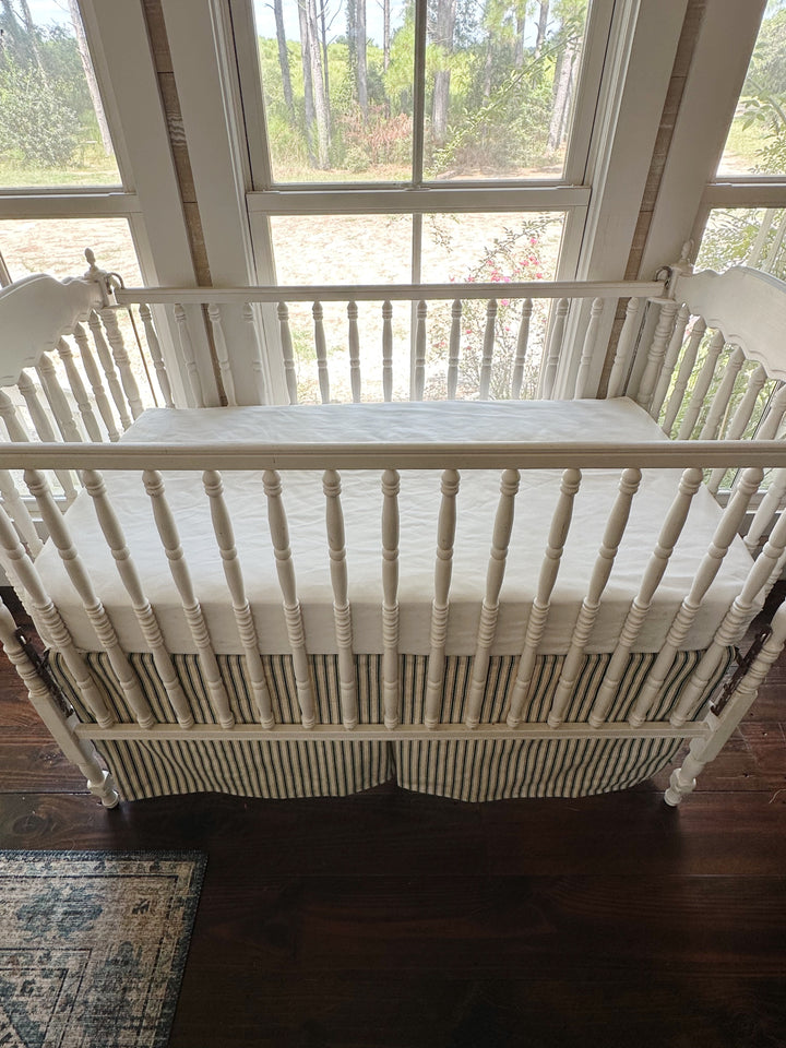 Looking down on the crib with the ticking skirt hanging below the white sheet