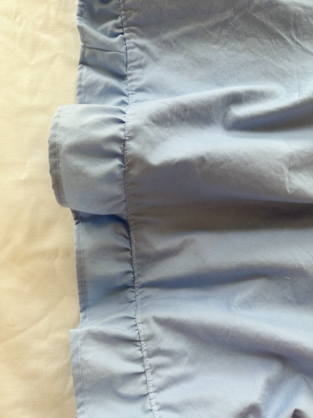 Detail of the hemmed ruffle and corner stitching on a baby blue washed cotton crib blanket - High Cotton Textile