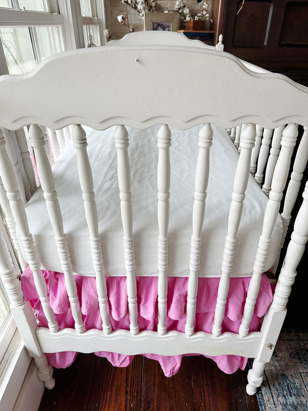 Foot of the crib with the parfait pink tiered skirt gathered beneath the scalloped end rail