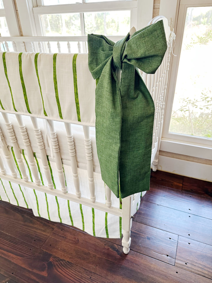 Green bow tied over the crib finial beside the striped rail cover
