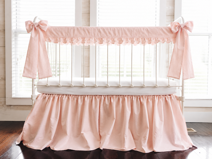 Ballet Slipper Pink ruffled crib rail cover, gathered farmhouse skirt and two long bows on a white iron crib, front view