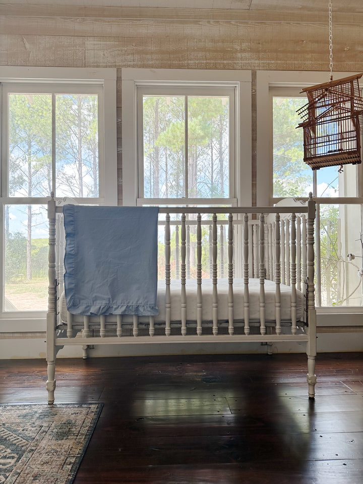 Baby blue ruffled crib blanket folded over the end of a white spindle crib in a pine-framed farmhouse nursery - High Cotton Textile