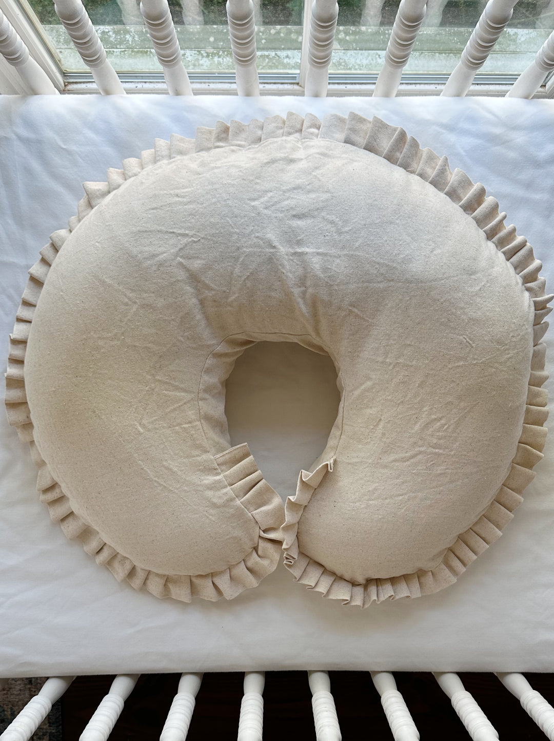 Natural Osnaburg ruffled Boppy pillow cover with a pleated ruffle, laid on a white crib mattress - High Cotton Textile