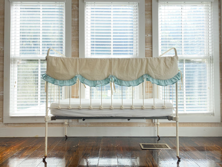 Antique white iron crib styled with an ivory and mist scalloped crib rail cover in a farmhouse nursery