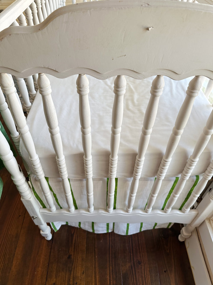 The scalloped headboard and turned spindles above the striped skirt's split corner