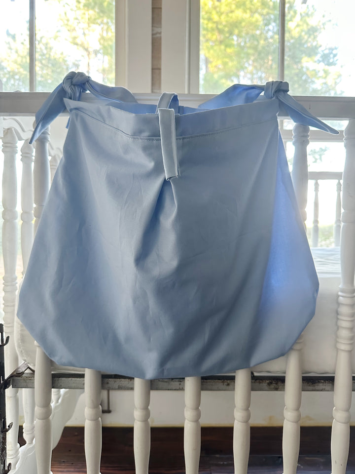 Baby blue tailored hanging crib caddy tied to a white crib rail with knotted cotton ties and a center tie at the top