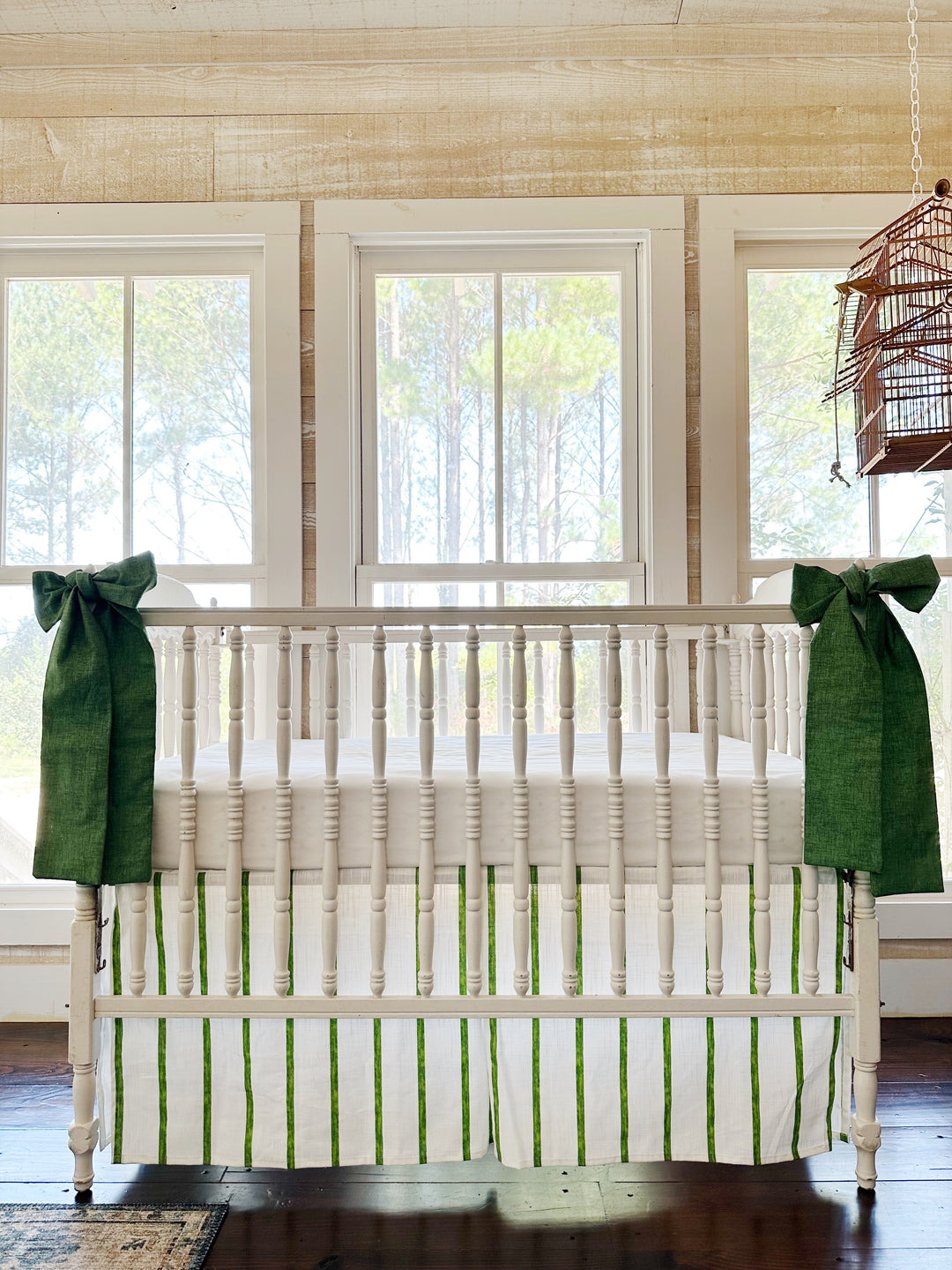 Cypress green and white striped tailored crib skirt with two solid green sashes tied to the front posts