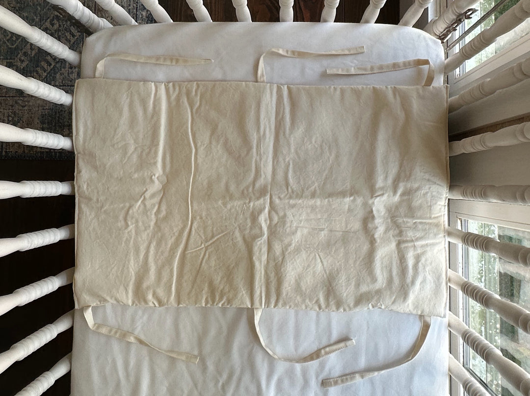 Natural crib rail cover laid flat across a crib mattress showing the cotton tie placement