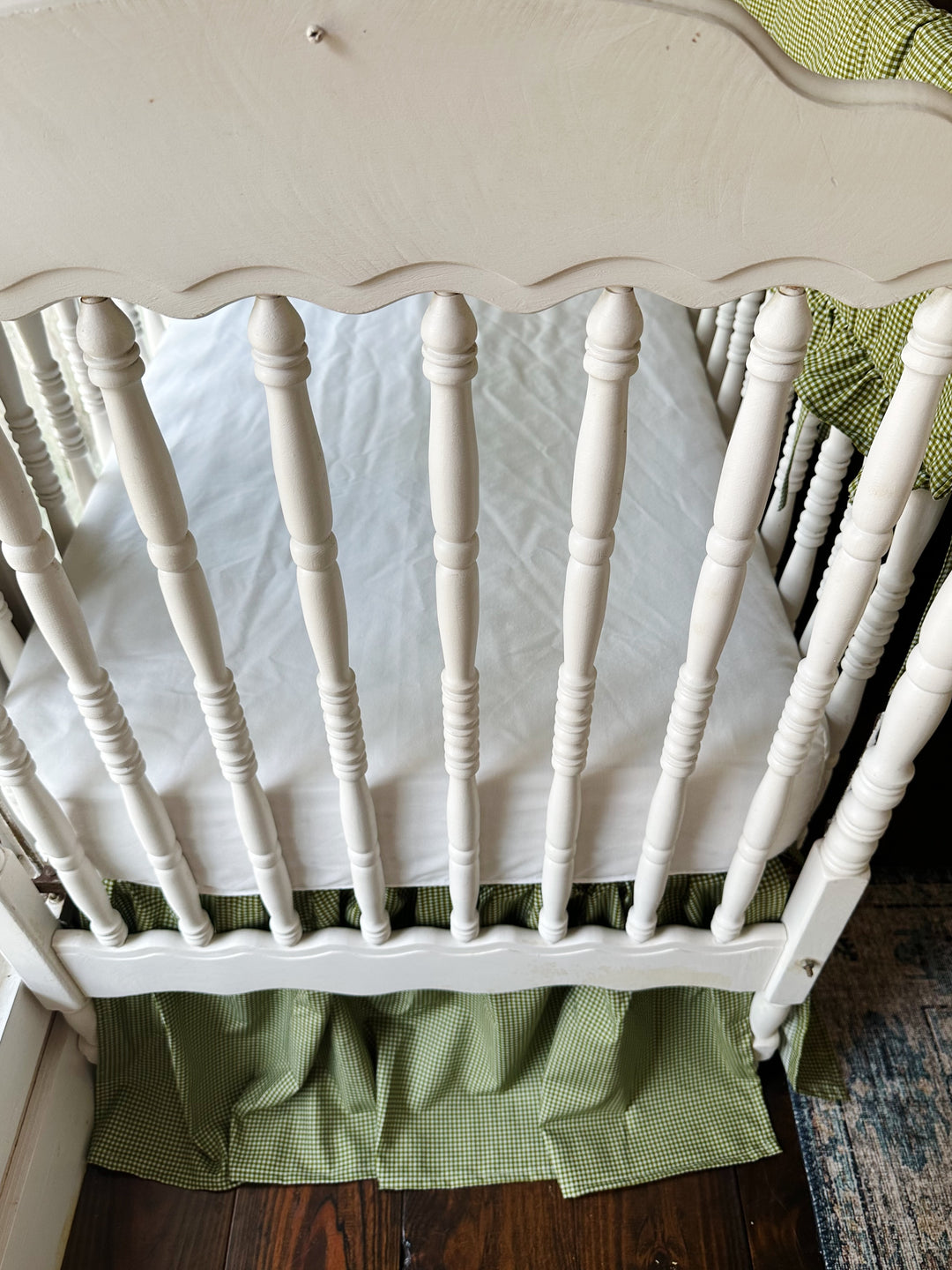 Overhead view of a white fitted crib sheet with the green gingham farmhouse crib skirt
