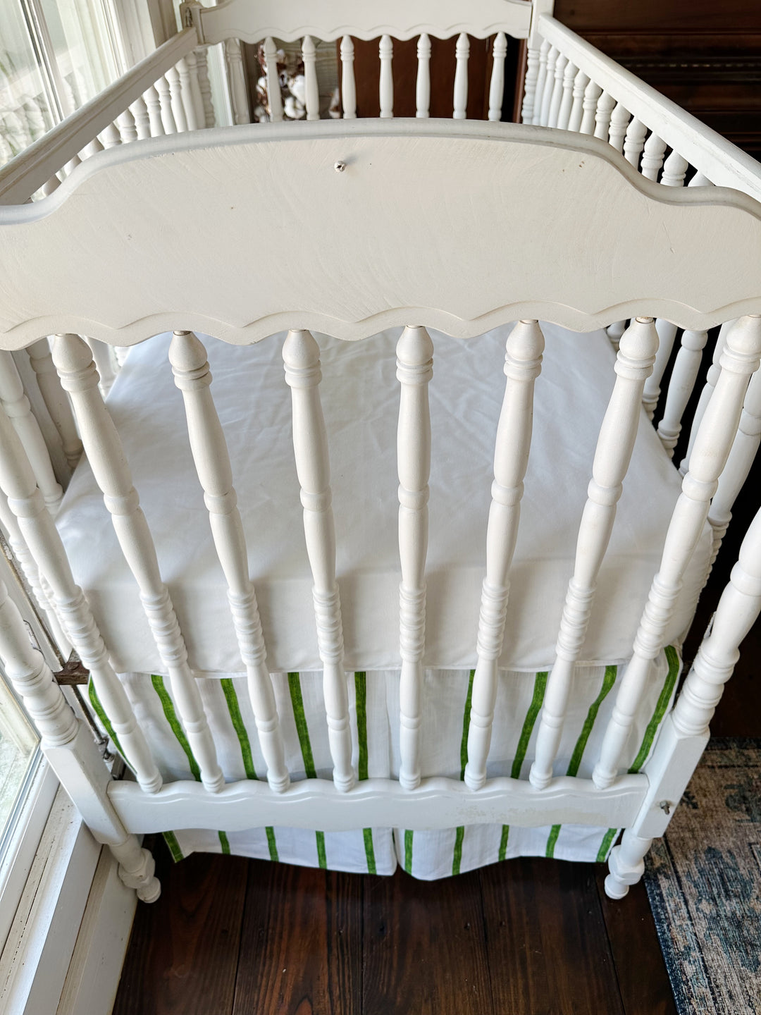 The scalloped headboard and spindles above the striped skirt at the head of the crib