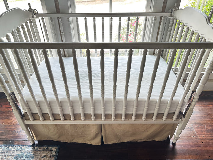 Oatmeal cotton crib skirt with center pleat styled on white heirloom crib - High Cotton Textile