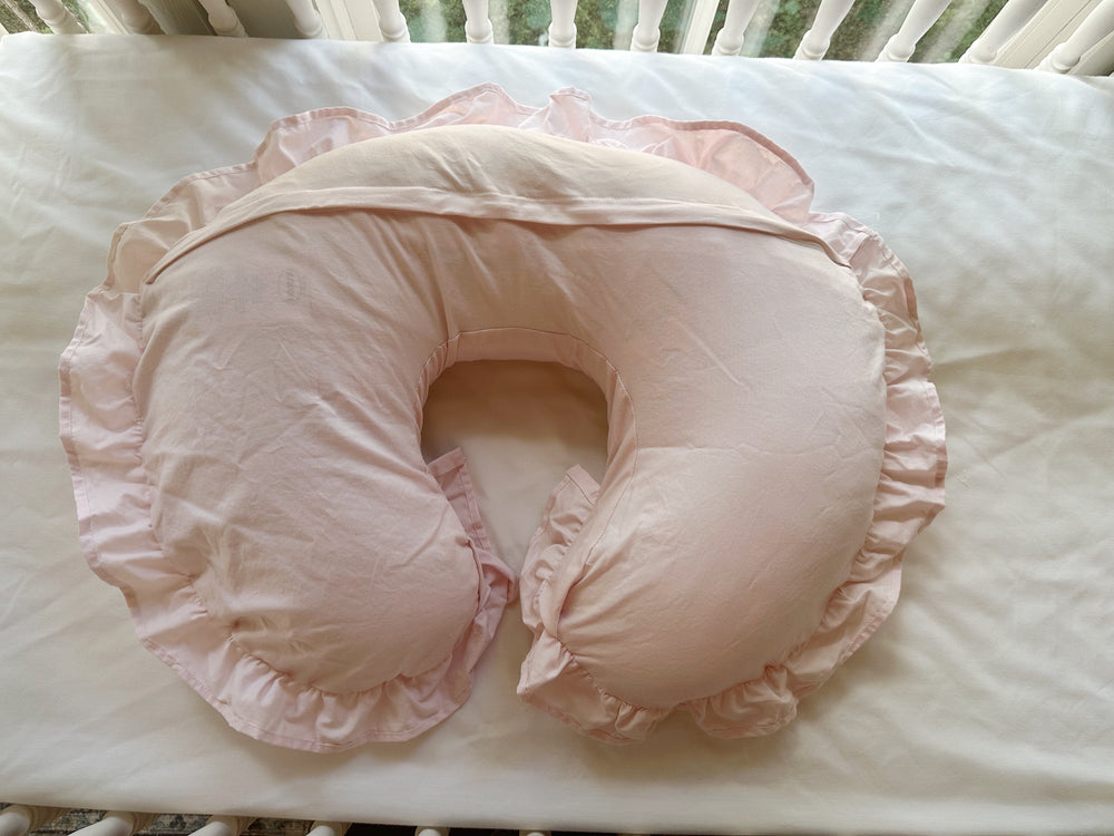 Back of the Baby Pink Boppy pillow cover in the crib, showing the envelope flap across the curve and the gathered ruffle
