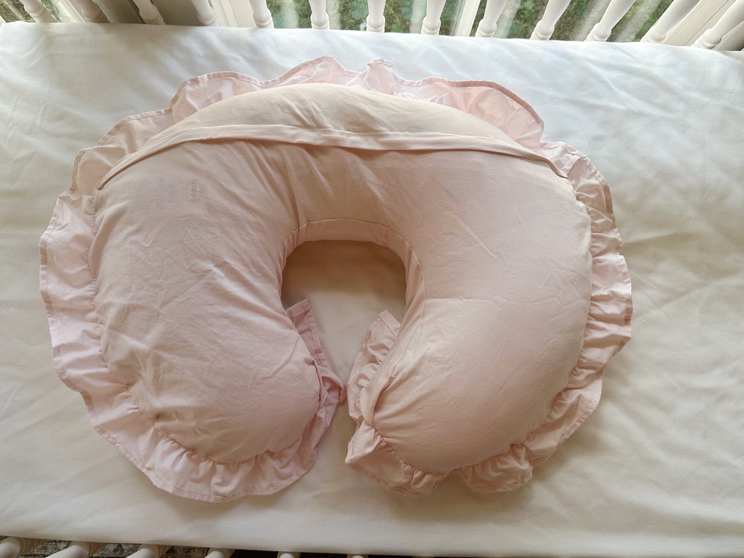 Back of the Baby Pink Boppy pillow cover in the crib, showing the envelope flap across the curve and the gathered ruffle