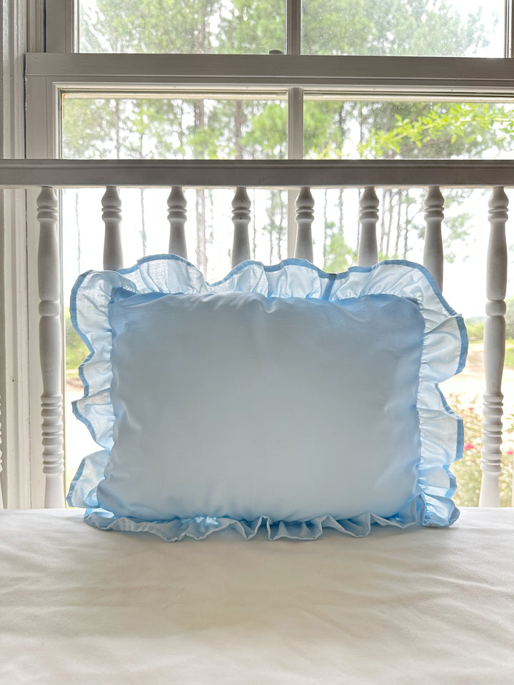 Light blue ruffled nursery pillow styled on a white spindle crib in a sunlit farmhouse nursery - High Cotton Textile