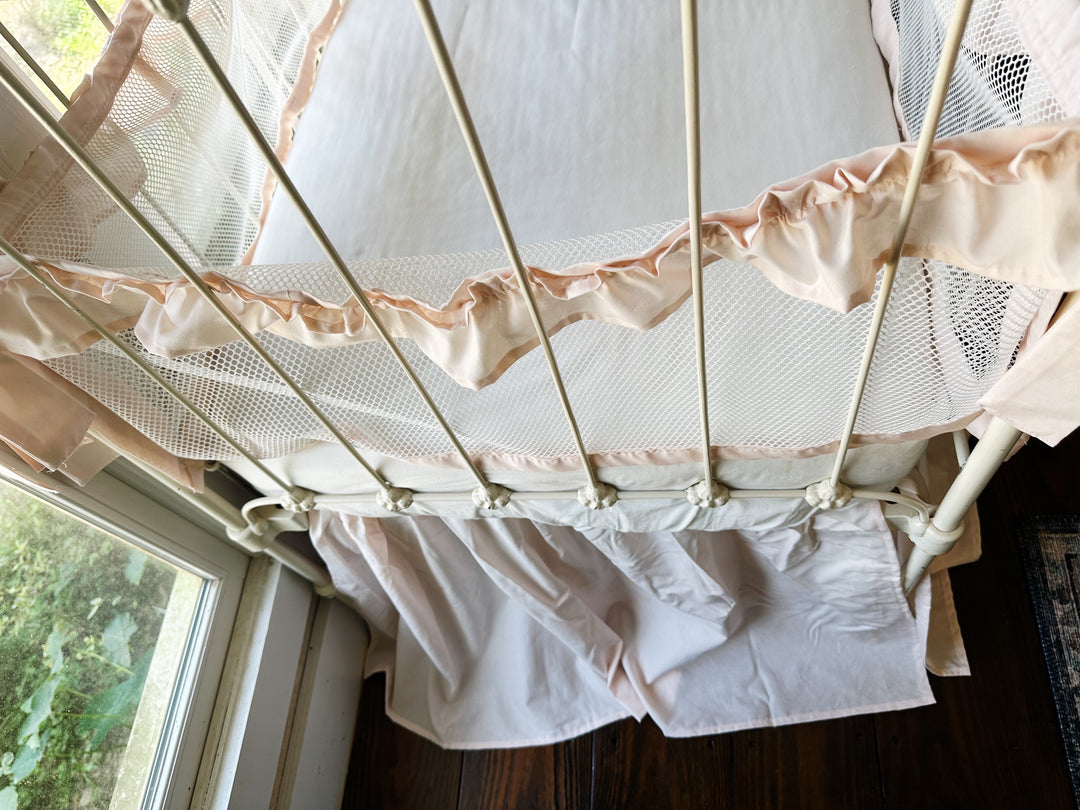 Side view of crib with full bedding set, showing liners tied to crib rails and skirt flowing around base
