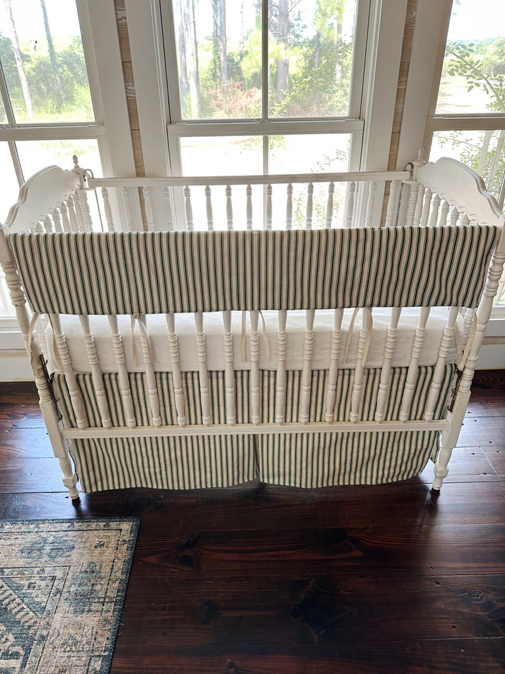 Looking down on the whole crib, the ticking rail cover and skirt against dark pine floors