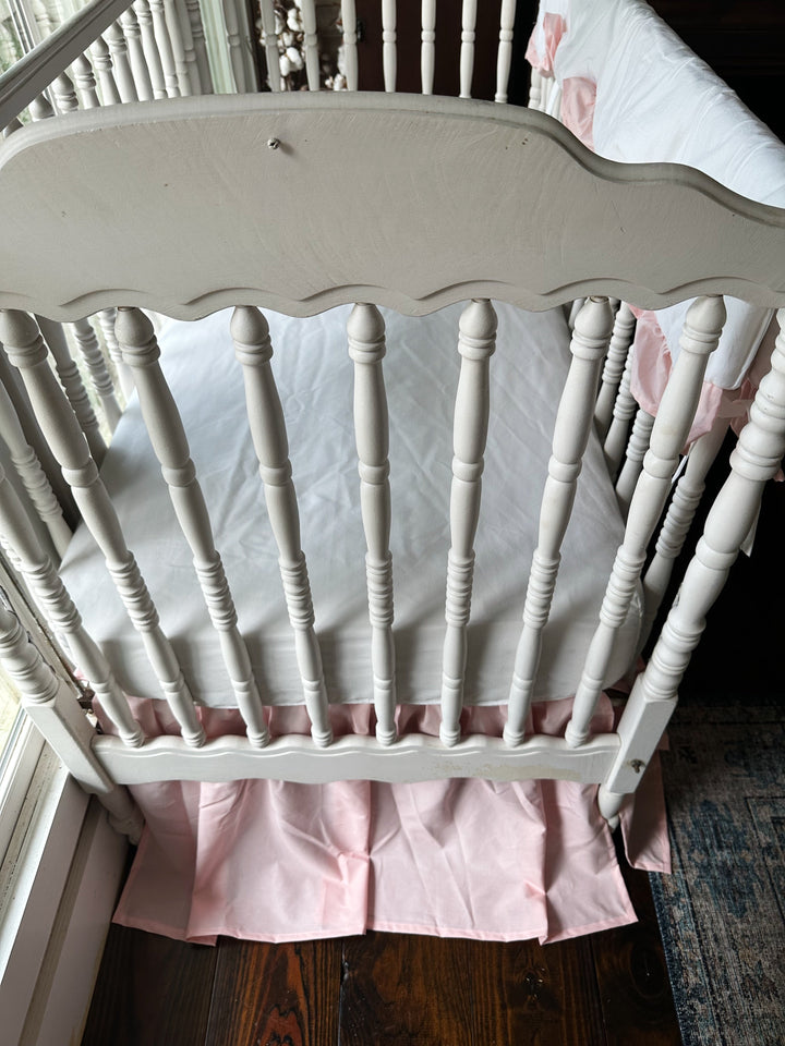 Sisters Pink farmhouse crib skirt and white fitted crib sheet seen from above inside a white crib