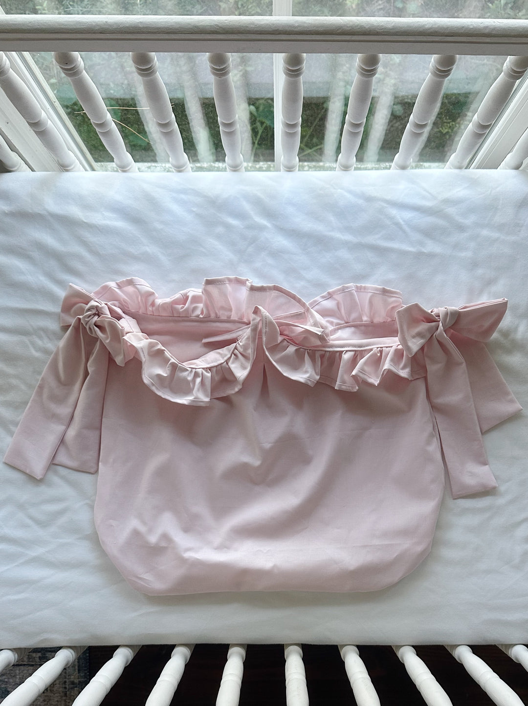 Baby pink ruffled crib caddy laid flat with its gathered ruffle opening and bow ties