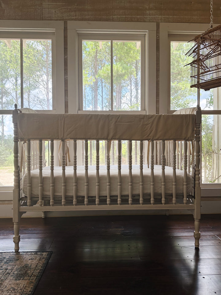 White spindle crib fitted with Natural neutral beige crib rail covers on every top rail