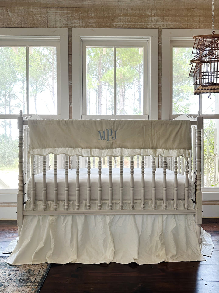 Monogrammed porcelain rail cover and gathered skirt seen from the front of the crib