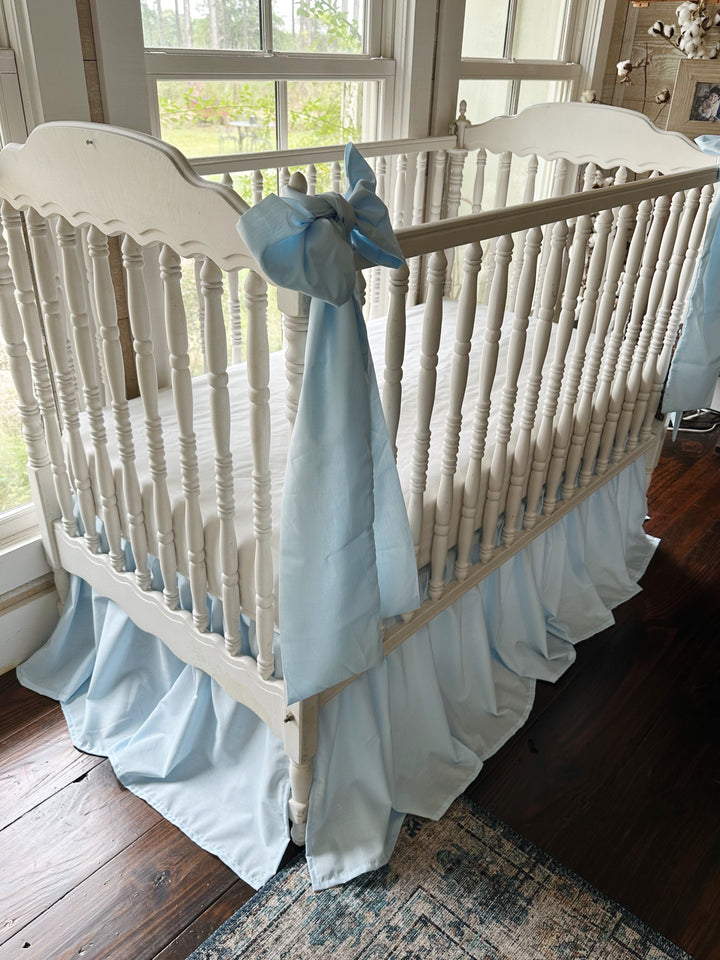 Angled view of the crib showing a bow at the corner post and the gathered blue skirt below
