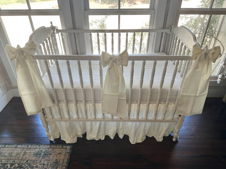 Porcelain crib skirt and bow set seen from standing height, three bows tied along the front rail of a white spindle crib