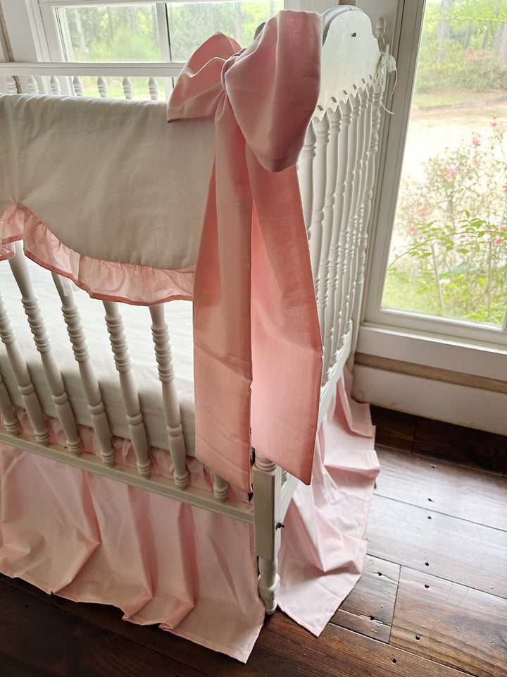 Side view of a Sisters Pink crib bow sash and the scalloped ruffle edge of the crib rail cover