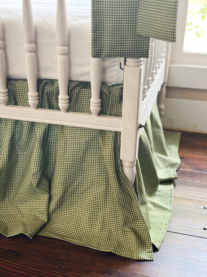 Corner detail of the green gingham crib skirt reaching toward a dark wood floor