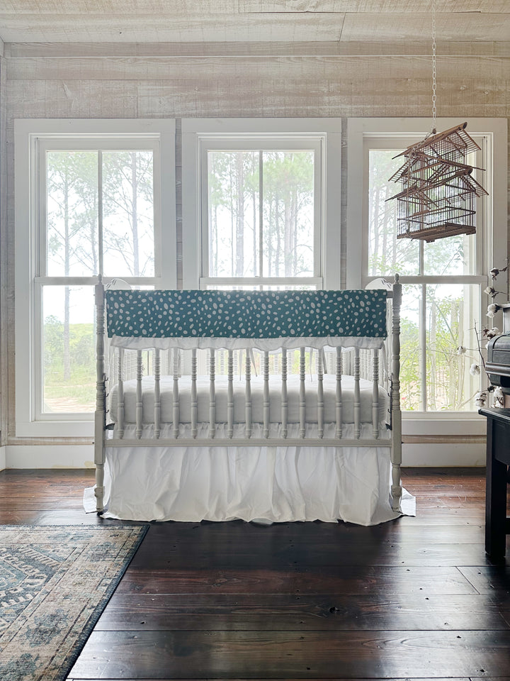 The two-piece green dot crib set in a pine-paneled nursery with three windows and a hanging birdcage