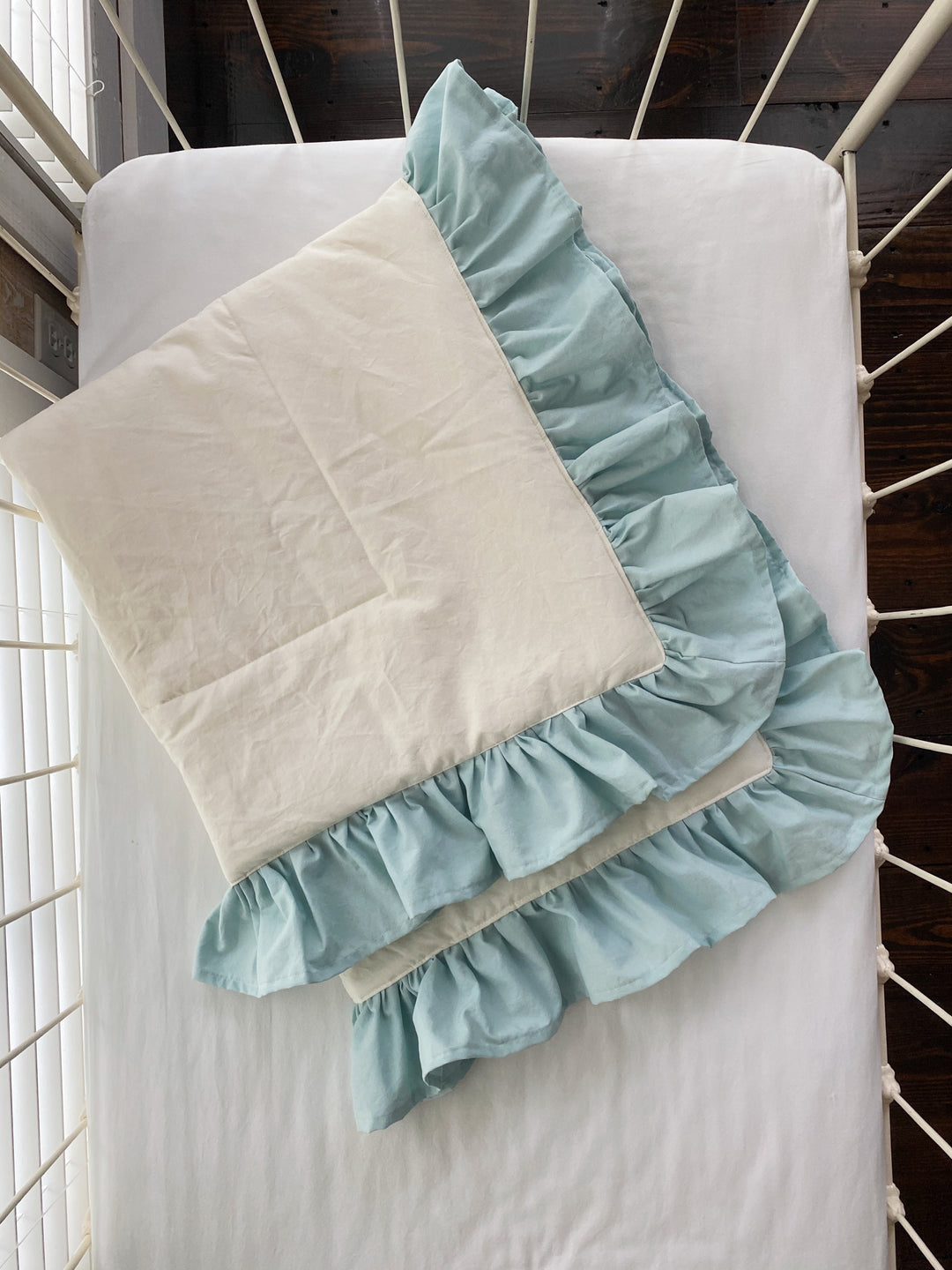 Ivory and mist ruffled baby quilt folded on a white crib mattress