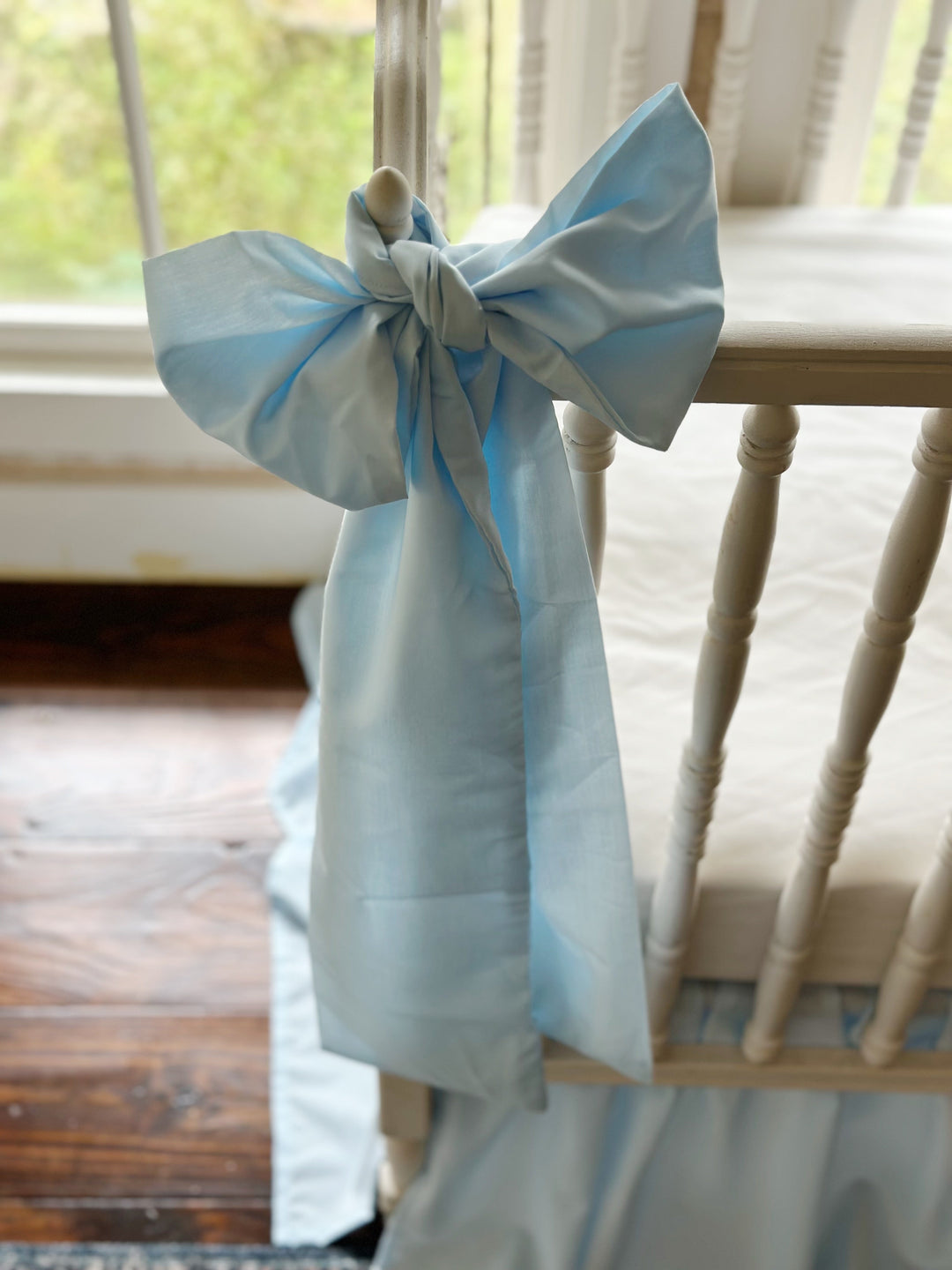 Heirloom blue bow on the crib rail above dark wood floors