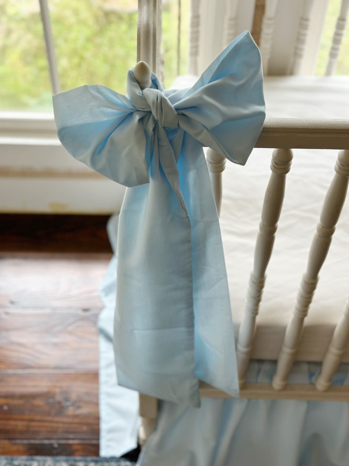 Heirloom blue bow on the crib rail above dark wood floors