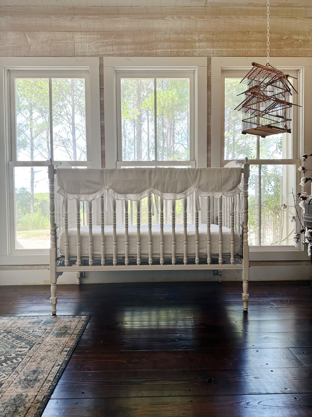 White scalloped crib rail cover styled on an heirloom crib in a bright farmhouse nursery