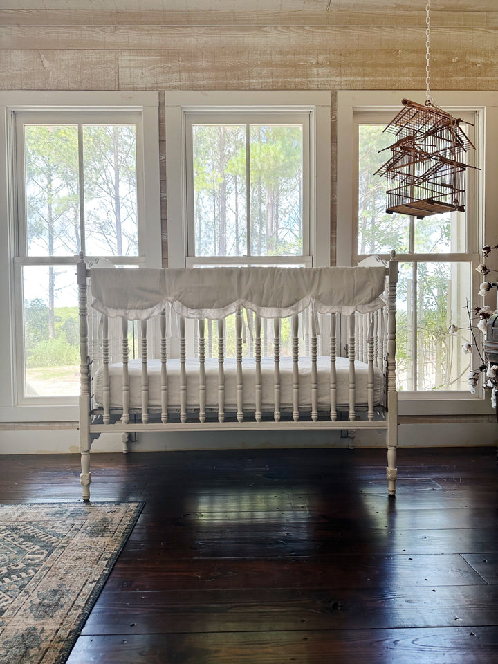 White scalloped crib rail cover styled on an heirloom crib in a bright farmhouse nursery
