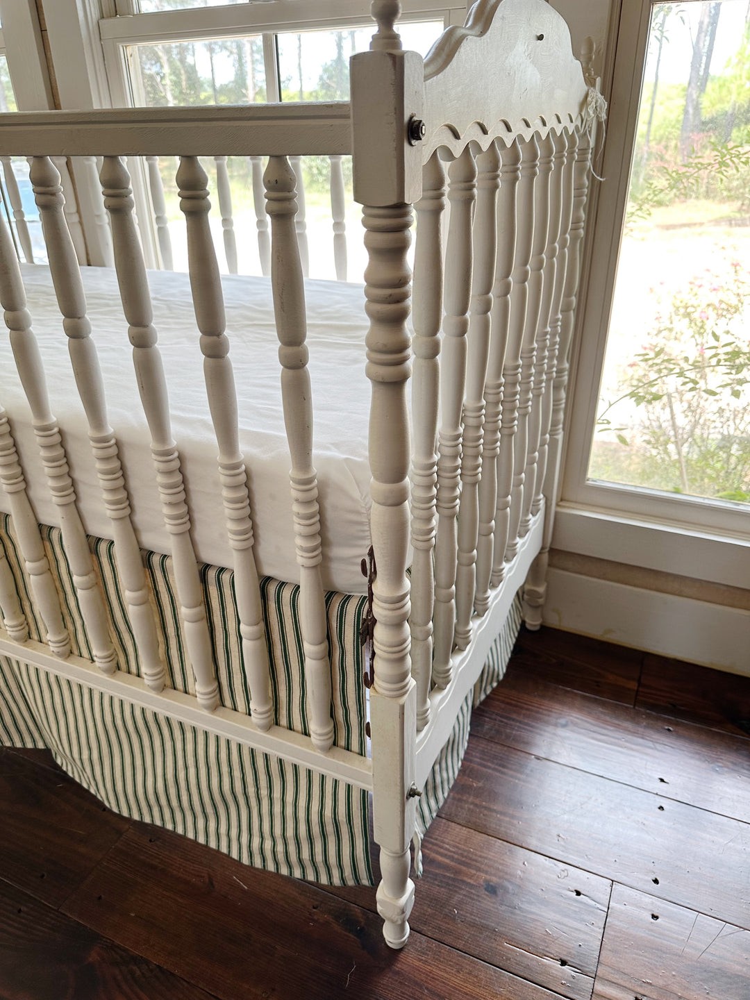 The corner of the crib where the ticking skirt wraps the leg, stripes running to the hem