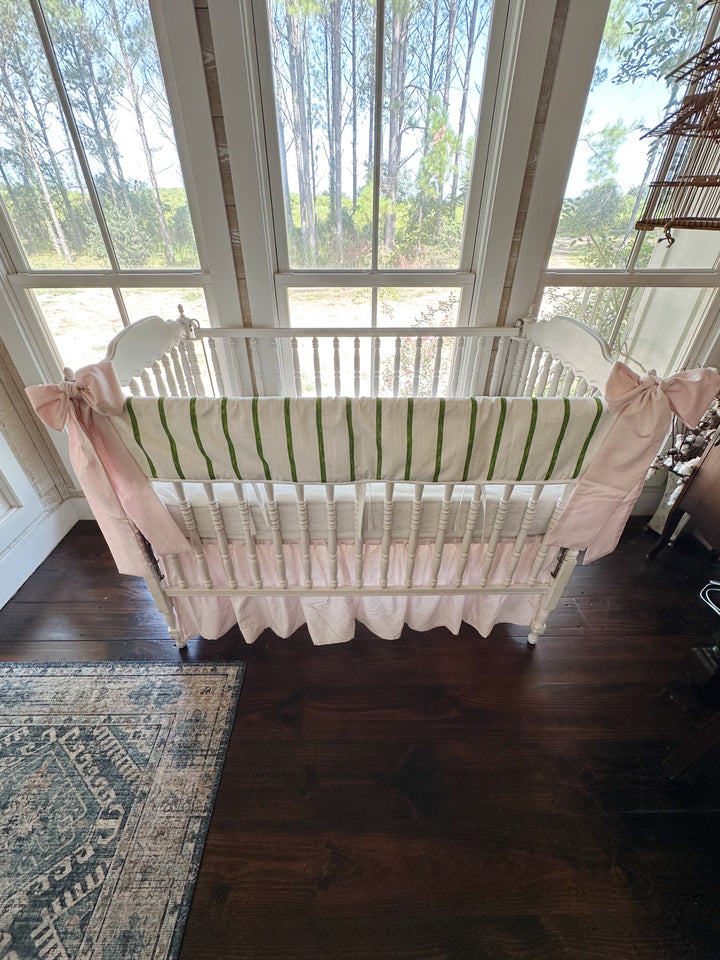 Overhead view of the whole crib showing the green stripe, white sheet and baby pink skirt