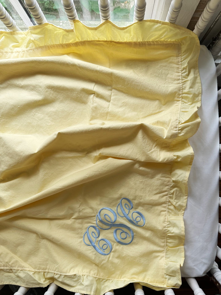 Close up of the ruffle edge and blue monogram on a handmade yellow cotton baby blanket - High Cotton Textile