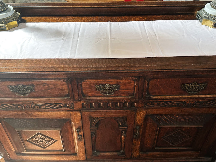 Baby pink cotton runner laid along the top of a carved oak sideboard between two marble and brass lamps