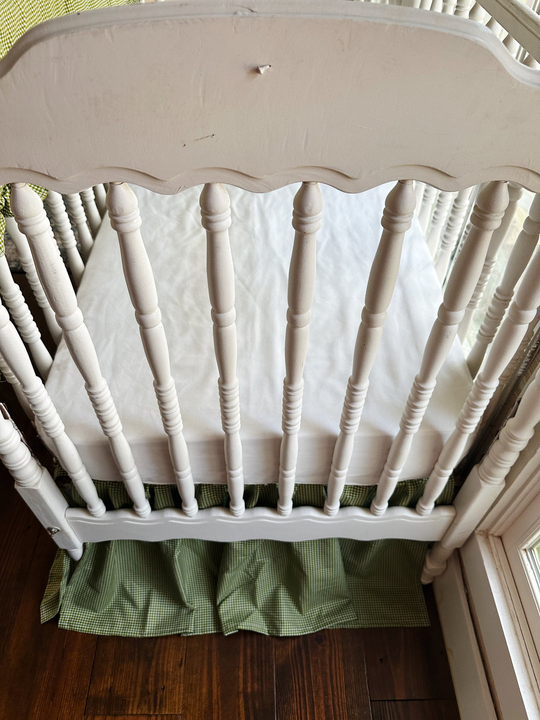 White spindle crib end with green gingham crib skirt and a white crib sheet