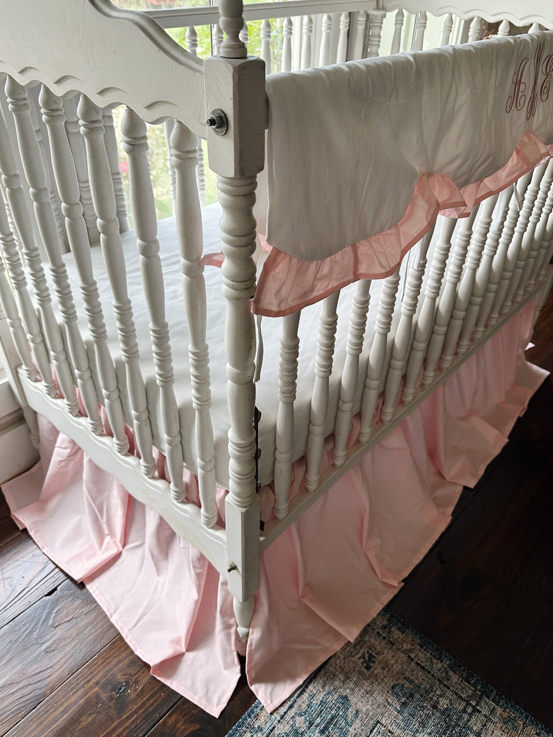 Corner view of the Sisters Pink crib rail cover and the pleated split corner of the farmhouse crib skirt