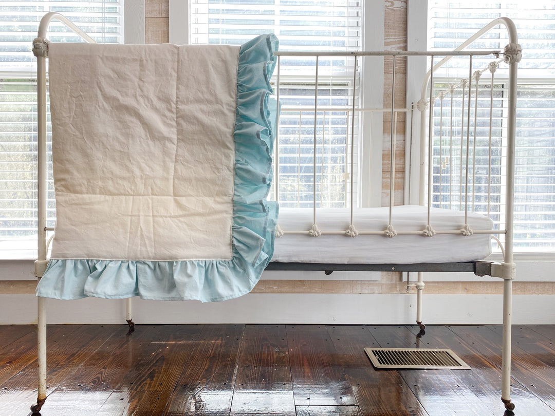 Ivory and mist ruffled baby quilt hung over the end of an antique white iron crib